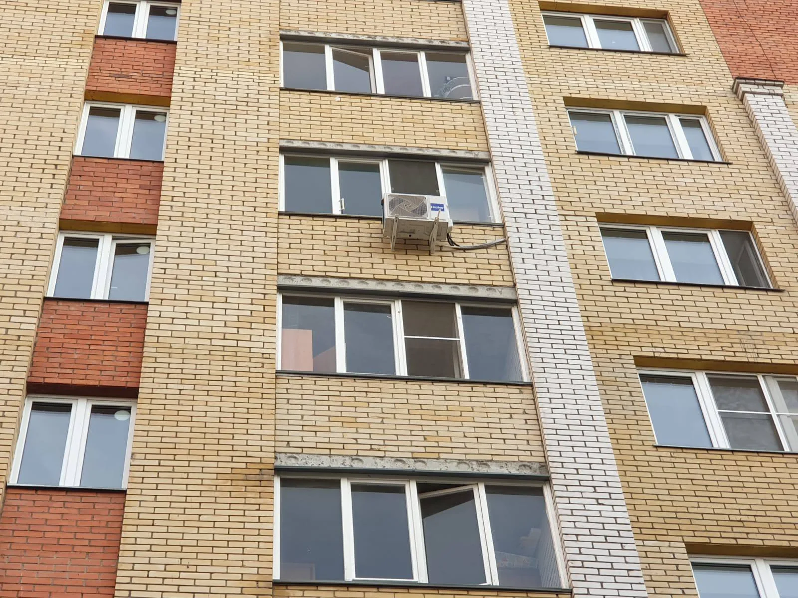 Общий вид наружного блока под окном на многоэтажном кирпичном фасаде