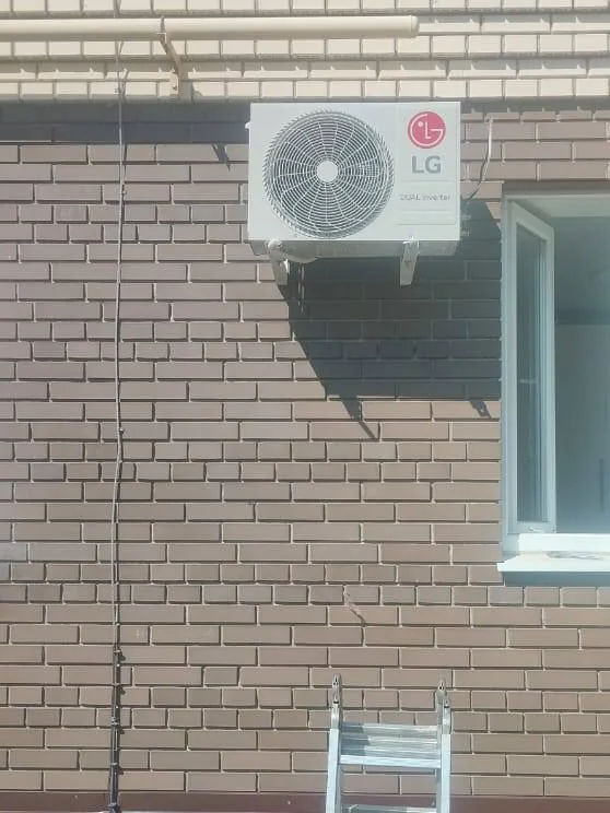 Наружный блок на кирпичном фасаде; под ним установлена приставная лестница