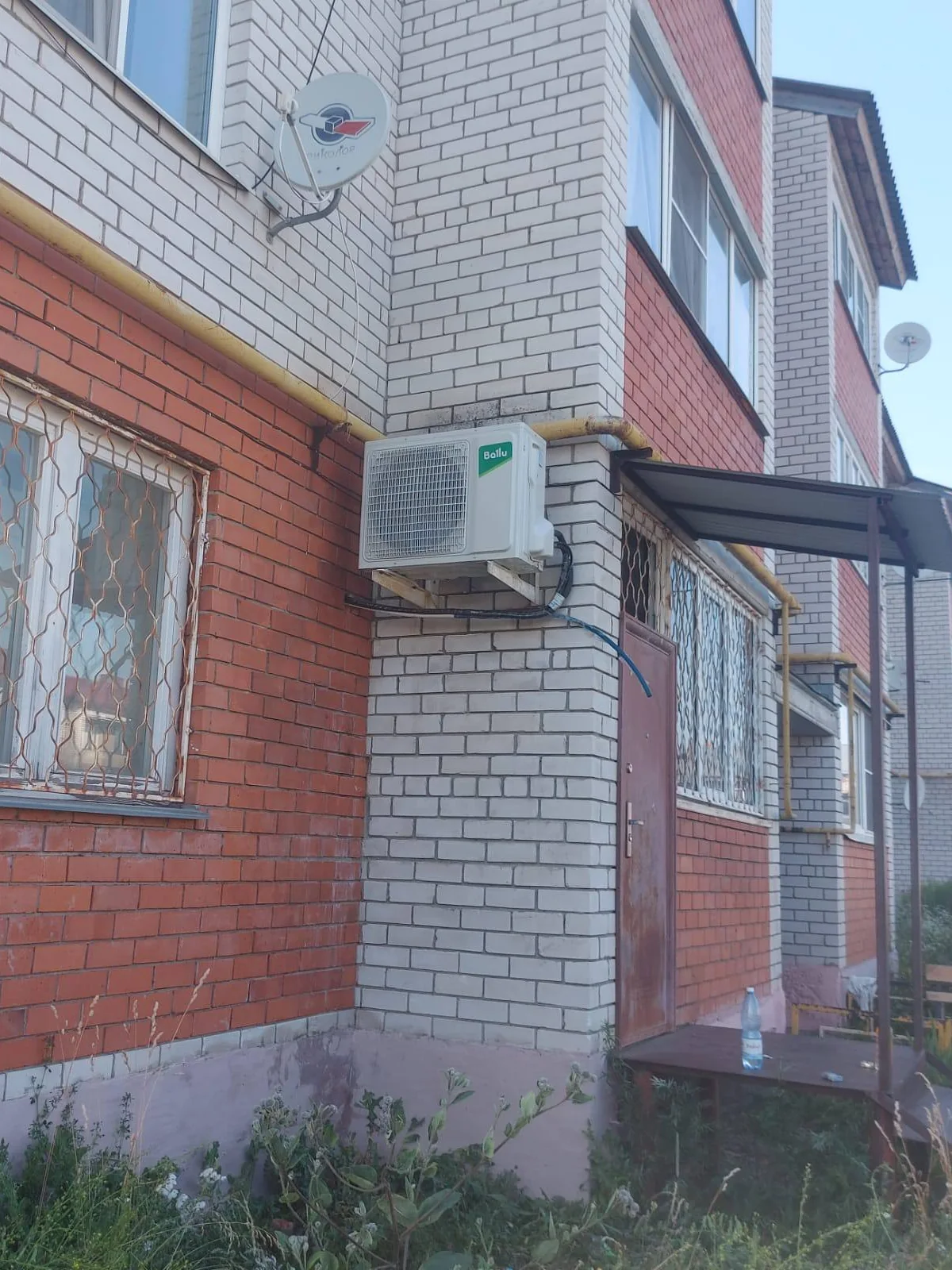 Наружный блок на углу красно-серого кирпичного фасада рядом с входным козырьком